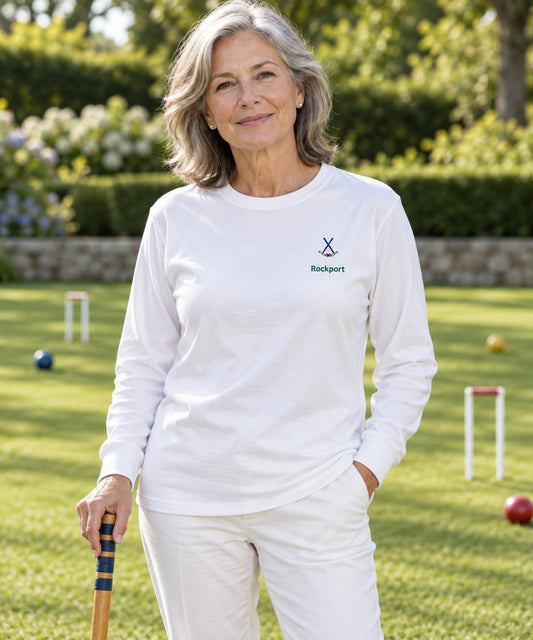 A woman standing on a green croquet lawn wearing a white long-sleeve t-shirt bearing a crossed mallets logo