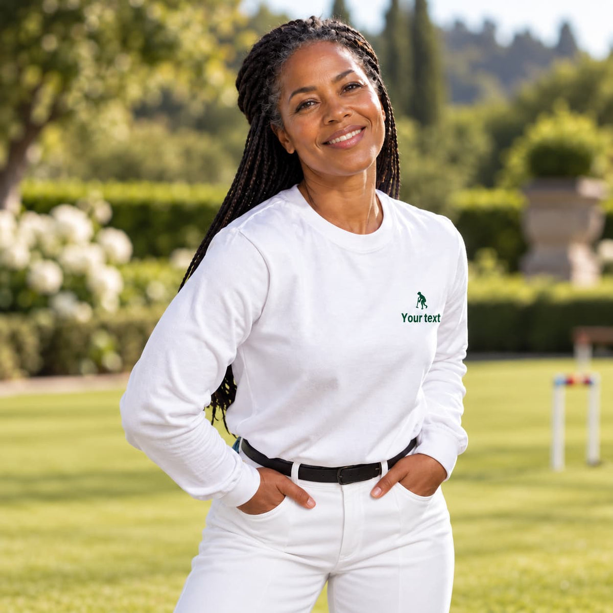 A woman wearing a white V-neck short-sleeve polo shirt with a green embroidered logo of a women striking a croquet ball on the left chest, standing outdoors on a sunny lawn.