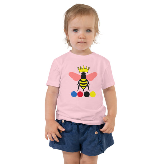 A toddler wearing a light pink short-sleeve T-shirt with a colorful queen bee graphic.